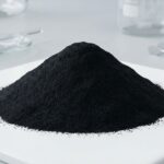 A mound of fine black iron oxide pigment powder in a laboratory, used for coloring plastics and rubber applications.