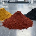 Vibrant mounds of iron oxide red, yellow, and black pigment powder in an industrial lab setting, used for permanent concrete coloring.