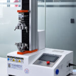 Universal testing machine with mechanical grips in a laboratory, used to measure tensile strength and elongation of cured epoxy samples.